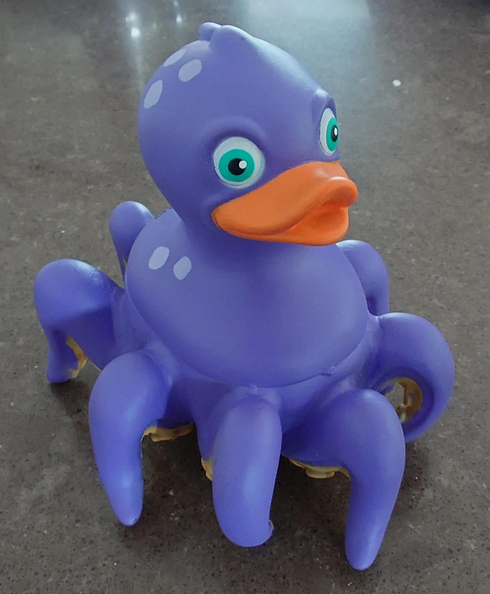 A photo of a purple toy with a duck on top and eight octopus legs on the bottom