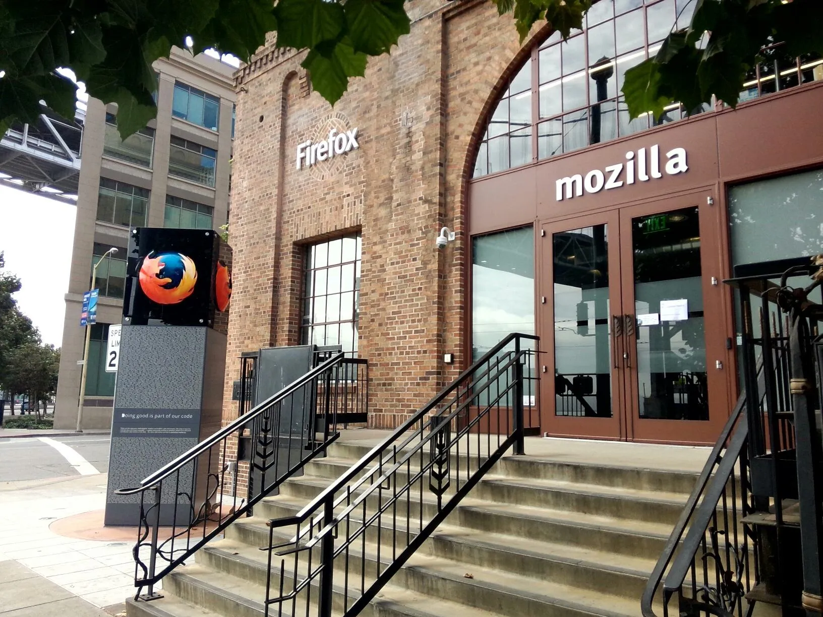 A building with a brick exterior, with "Mozilla" written above the main entrance and a "Firefox" logo on the wall next to it. On the left side of the door stands a decorative column with a three-dimensional Firefox flame fox icon on it and densely engraved words below.